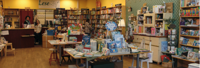 Eingangsbereich der Buchhandlung LeseZeit in Bad Vilbel-Dortelweil mit Blick auf die Büchertische und die gemütliche Sitzecke.