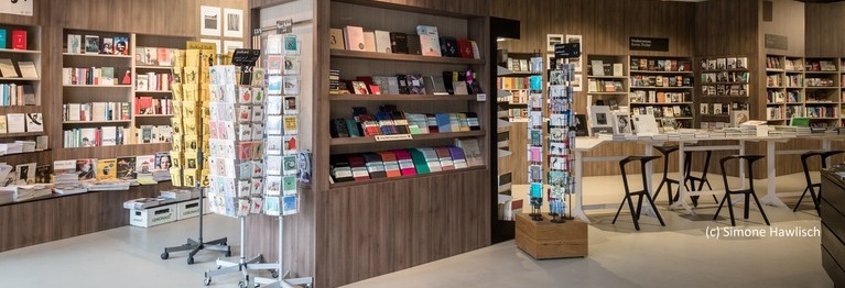 Vorderer Bereich der Buchhandlung mit Postkartenständern und Regalen.