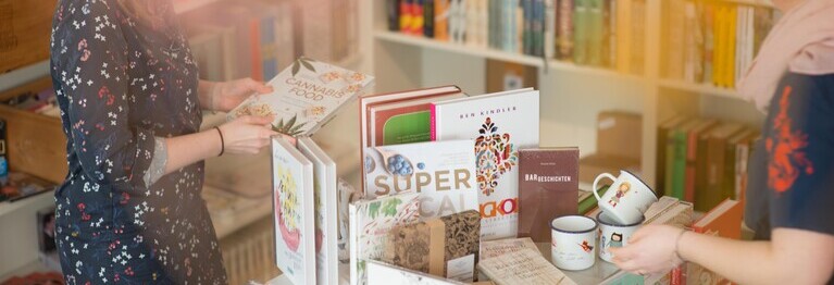 zwei Buchhändlerinnen sortieren Bücher auf einen Tisch