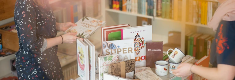 zwei Buchhändlerinnen sortieren Bücher auf einen Tisch