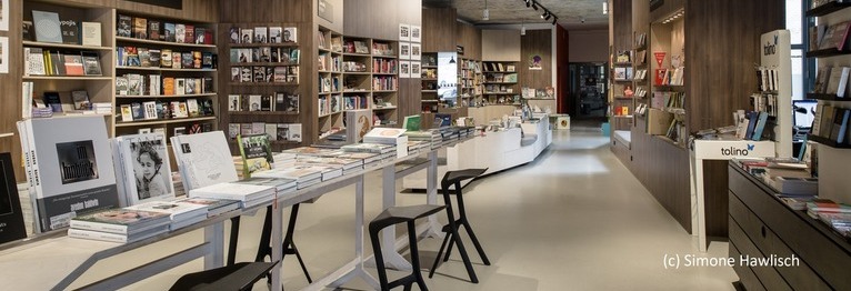 Ein Ausschnitt des Ladeninneren. Zu sehen ist ein langer Tisch mit Büchern darauf und Bücherregale.